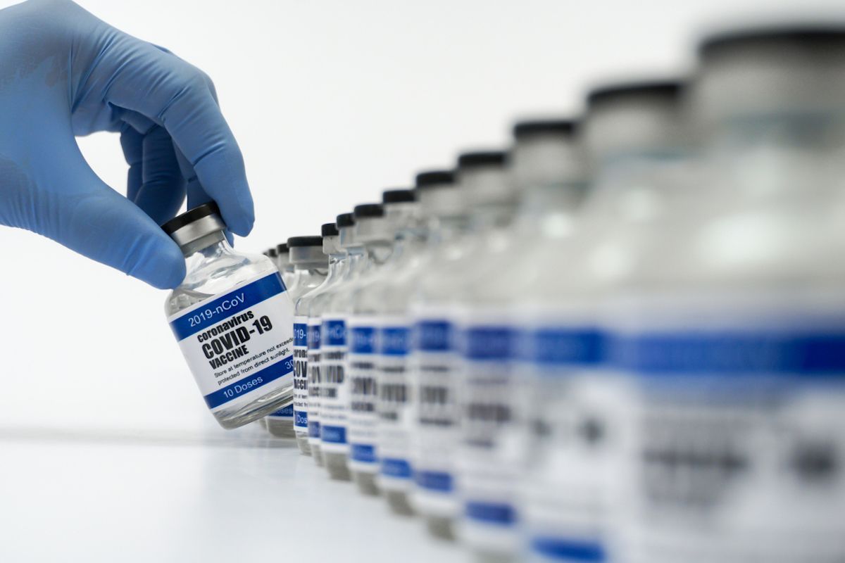 Covid-19 vakcinos buteliukas paimtas mėlynomis nitrilo chirurginėmis pirštinėmis dengta ranka