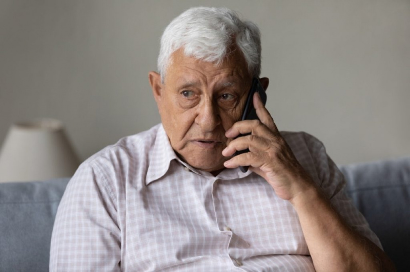   възрастен мъж, изглеждащ притеснен и загрижен, провеждайки телефонно обаждане на дивана си