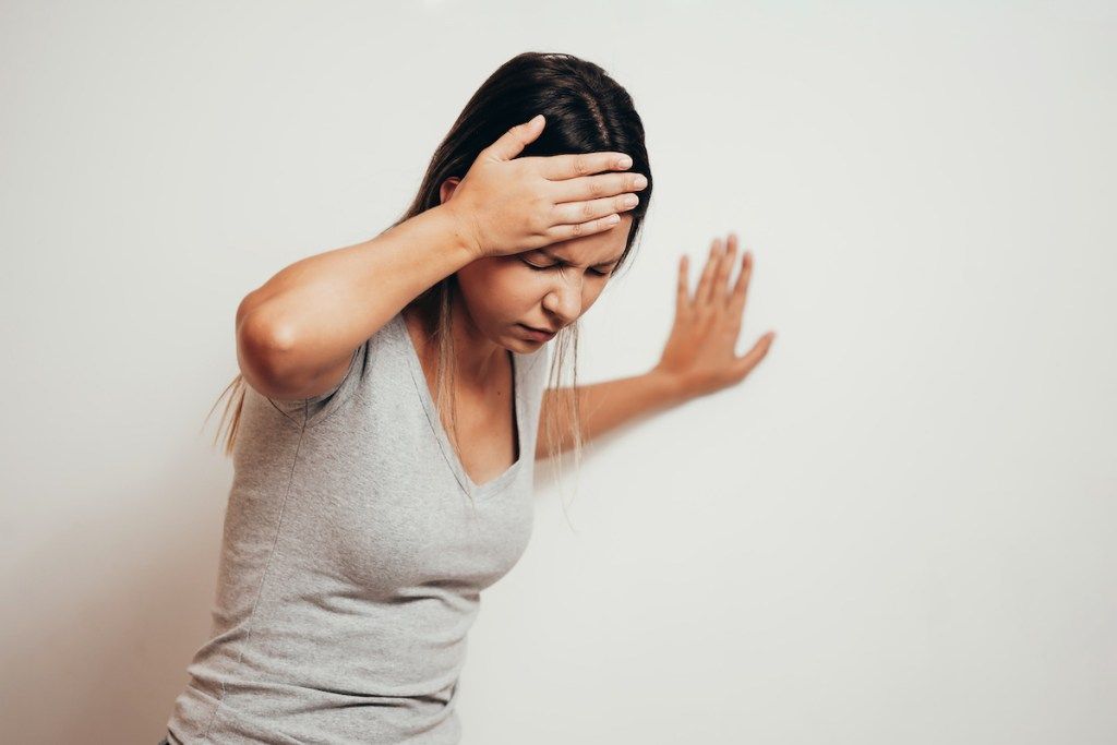 Жена, страдаща от световъртеж с трудности при изправяне, докато се опира на стената