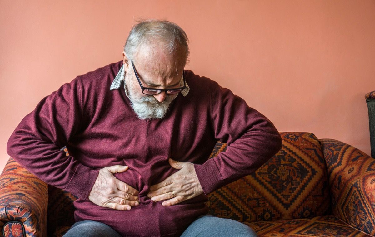 Възрастен мъж опъва подутия си стомах в дискомфорт