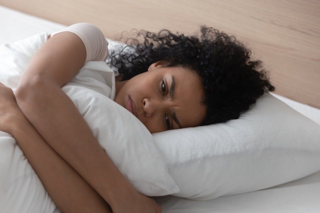 donna triste sdraiata a letto abbracciando il suo cuscino