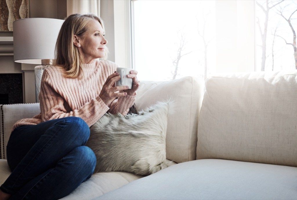 nő ül egyedül a kanapén kávét kortyolgatva