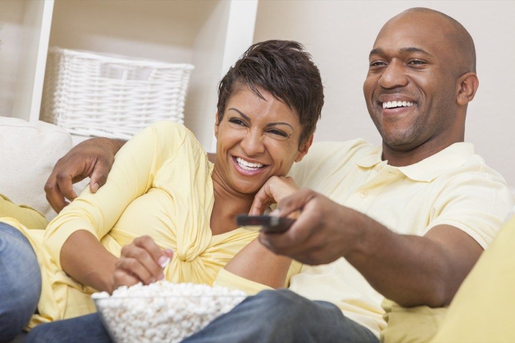 Черна двойка, гледаща телевизия с дистанционно на дивана