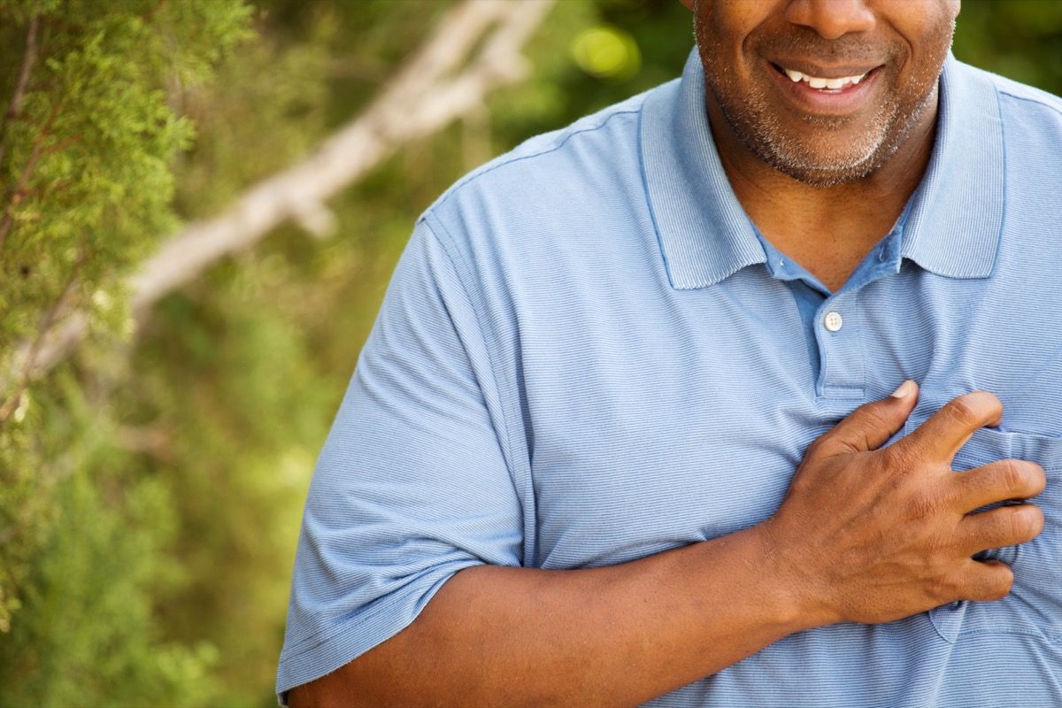 Schwarzer Mann legt Hand auf die Brust wegen saurem Reflux, Dinge, die Ihren Zahnarzt entsetzen würden