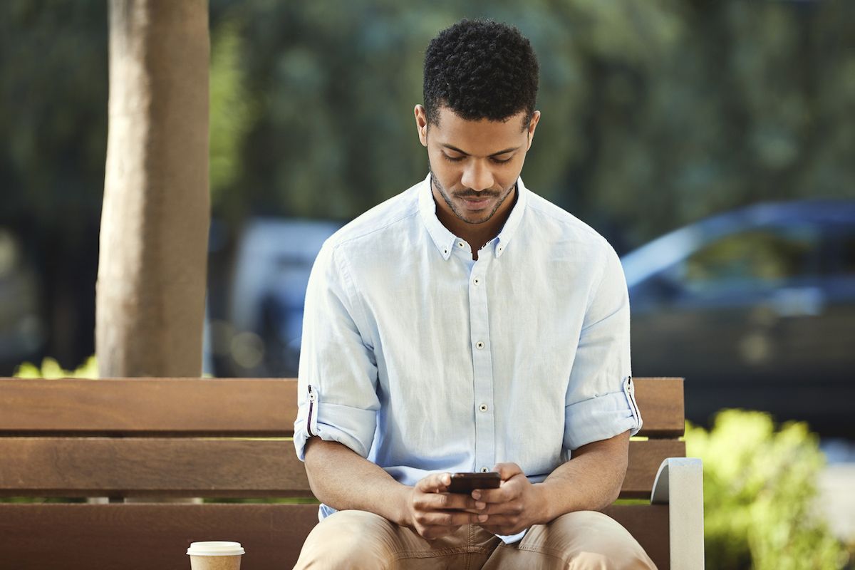 Młody człowiek za pomocą telefonu komórkowego, siedząc na ławce