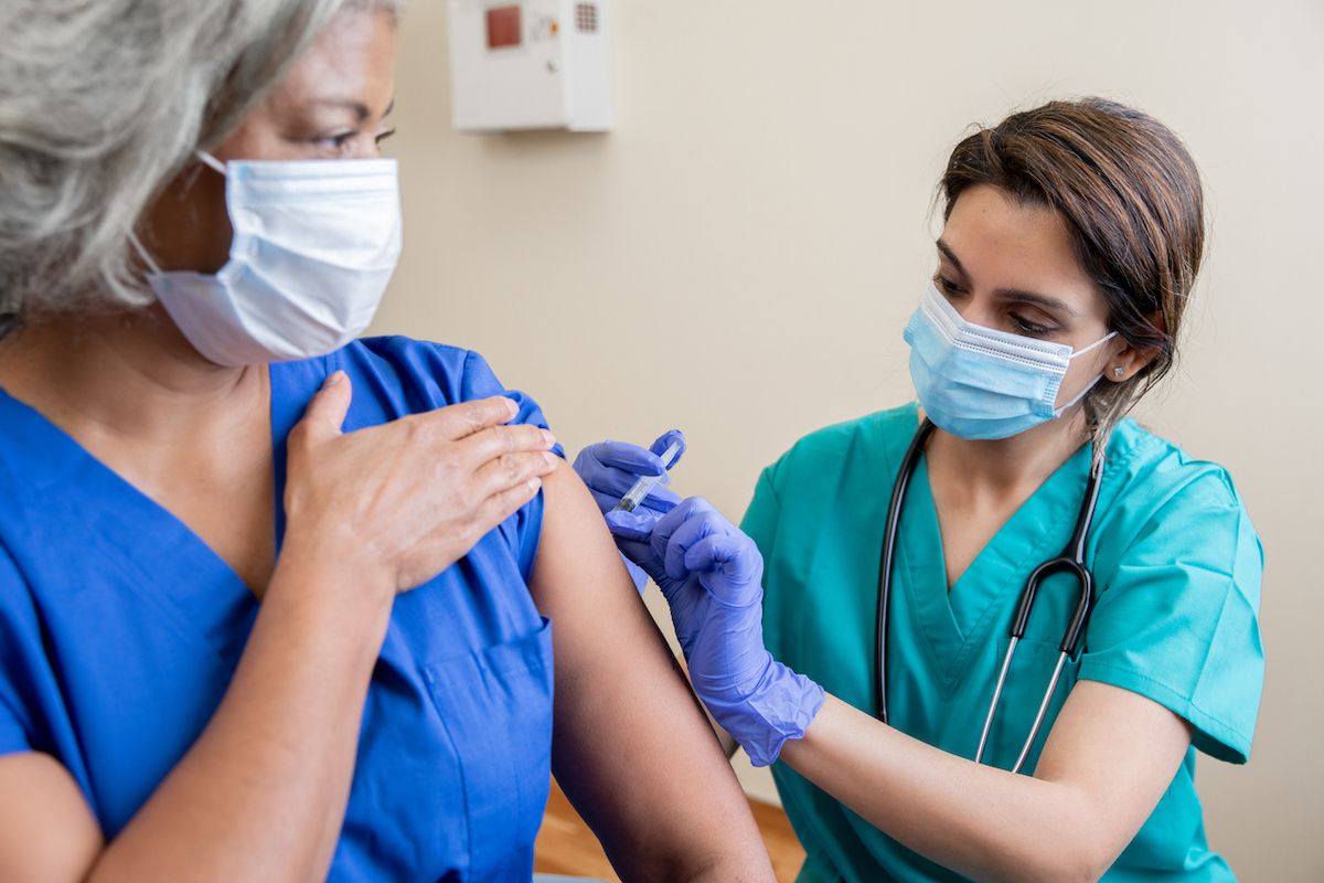 Krankenschwester gibt älteren erwachsenen Gesundheitspersonal den Covid-19-Impfstoff