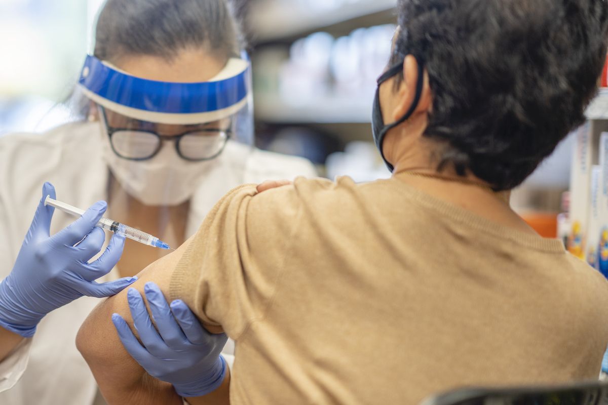 Una dona enmascarada prenent una vacuna mentre estava a la farmàcia per una dona farmacèutica.