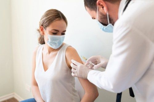 Nærbilde av en nervøs kvinne og legen hennes som bærer ansiktsmasker og får COVID-vaksinen