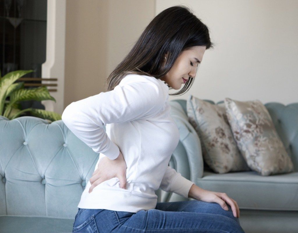 Sieviete ar muguras sāpēm aizturot sēdus dīvānā
