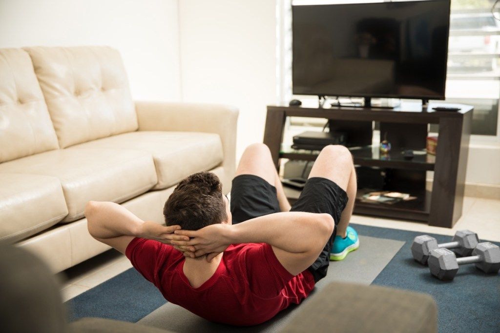 Bărbat care face croșete în fața televizorului din sufragerie
