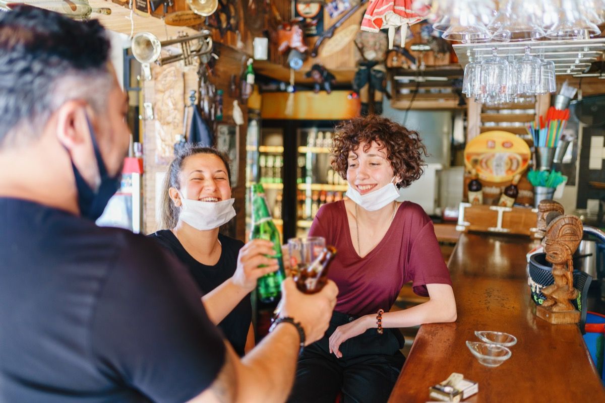 Las personas vitoreando con cerveza en el bar con medidas de protección para la prevención de enfermedades se toman