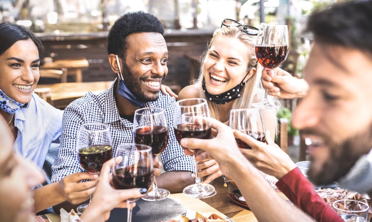 Amigos brindando vino tinto en el bar restaurante al aire libre con mascarilla abierta - Nuevo concepto de estilo de vida normal con gente feliz divirtiéndose juntos en un filtro cálido