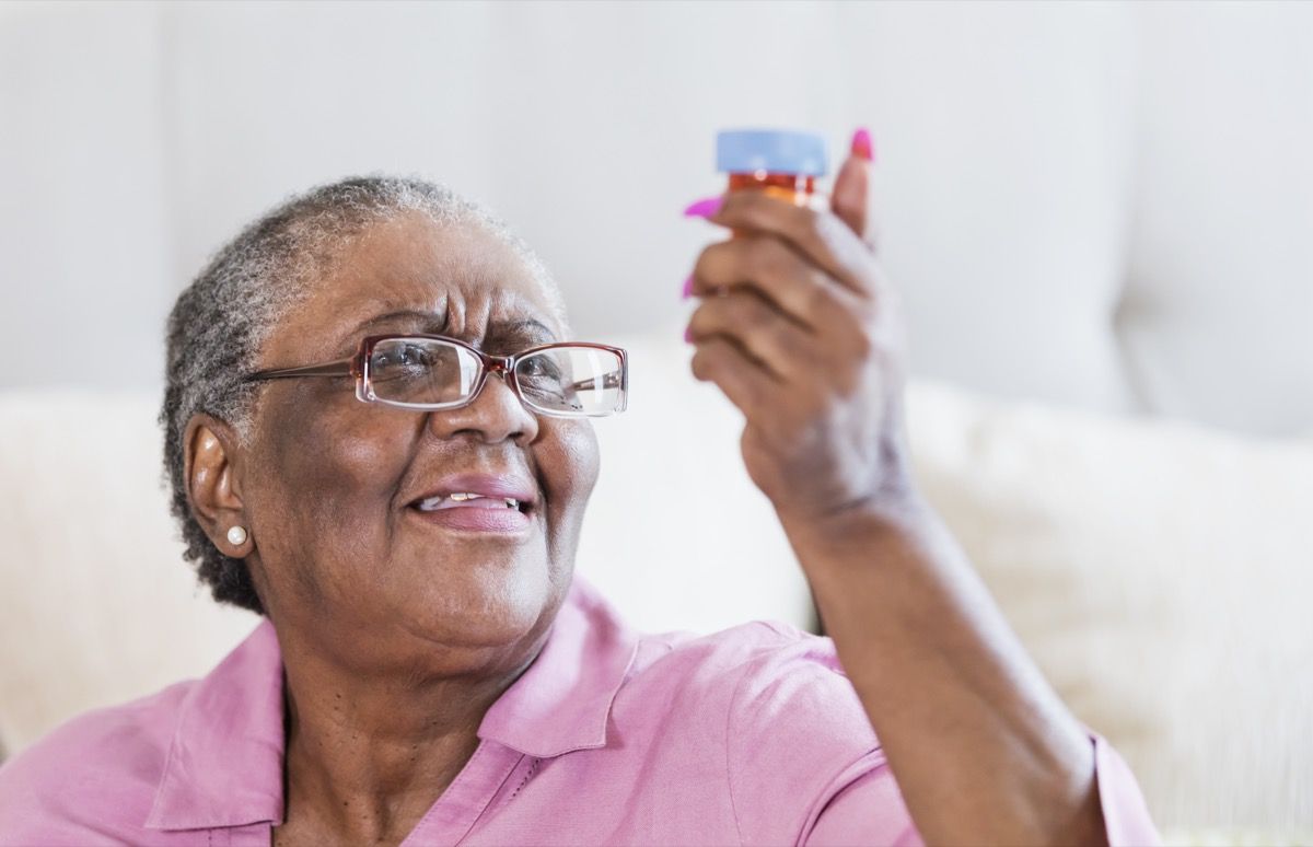 Mulher afro-americana idosa com dificuldade para ler o rótulo de um medicamento