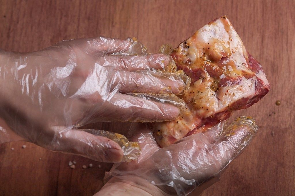 χέρια με γάντια μαρινάροντας ένα κομμάτι κρέας
