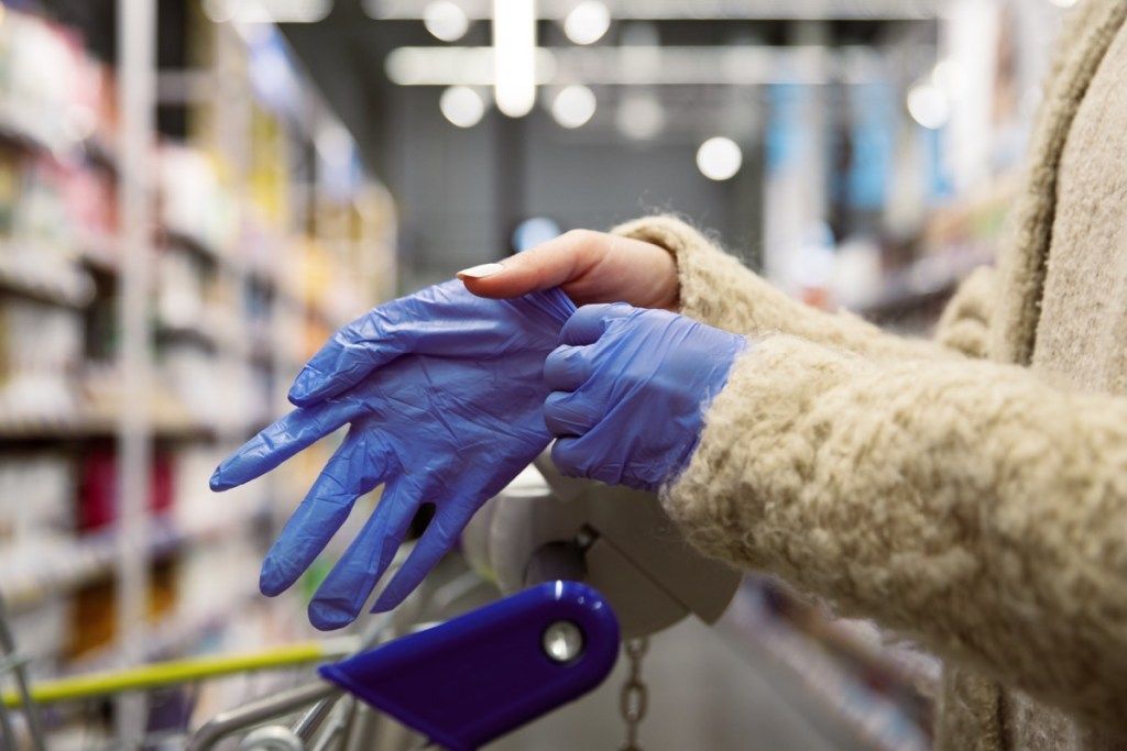 žena stavlja rukavice u prolazu supermarketa
