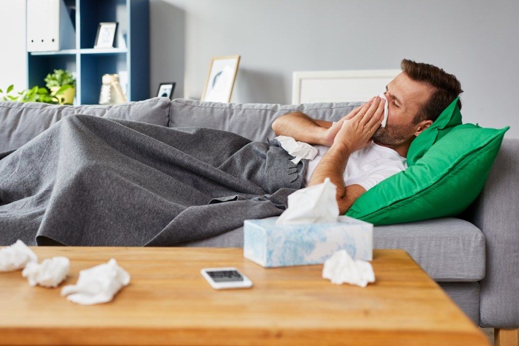Žmogus su peršalimu ant sofos pučia nosį