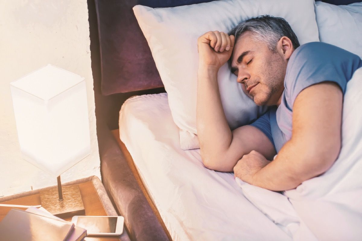 middelaldrende hvit mann som sover i blå t-skjorte ved siden av lampen