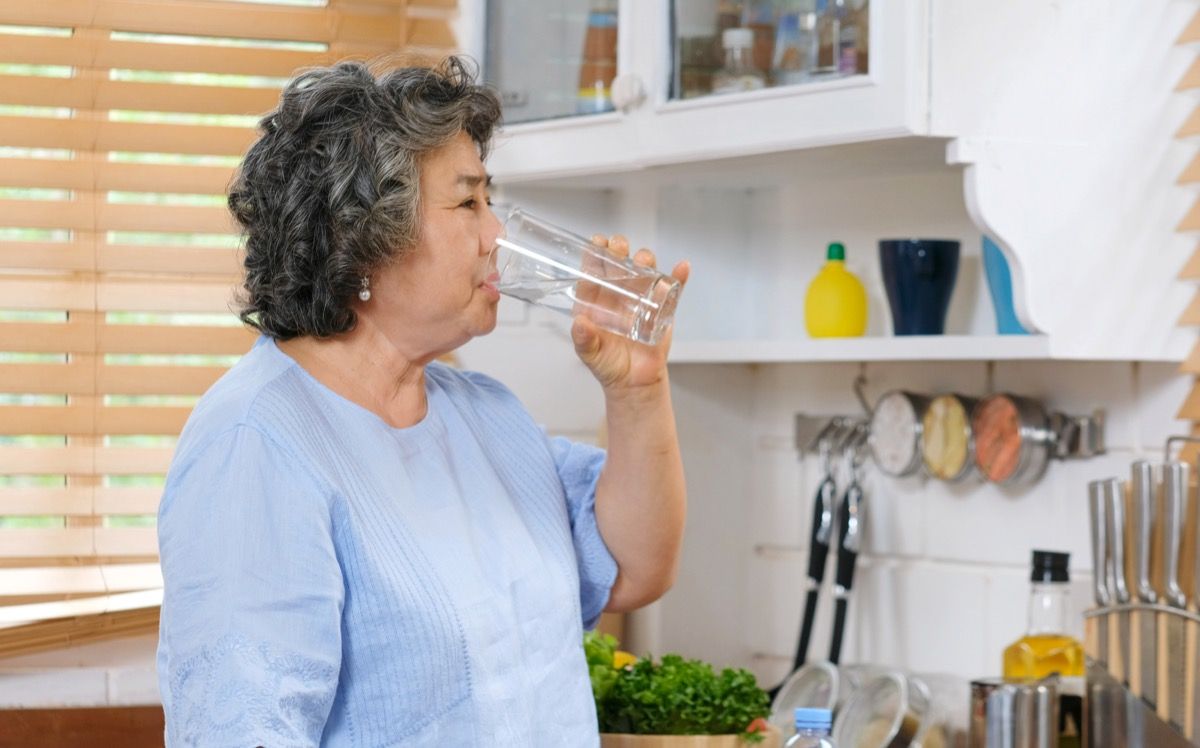 Yaşlı Asyalı kadın mutfakta su içme
