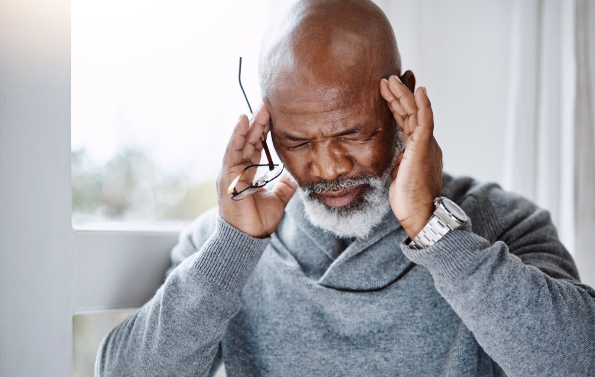 Foto de um homem idoso sofrendo de dor de cabeça em casa e parecendo estressado