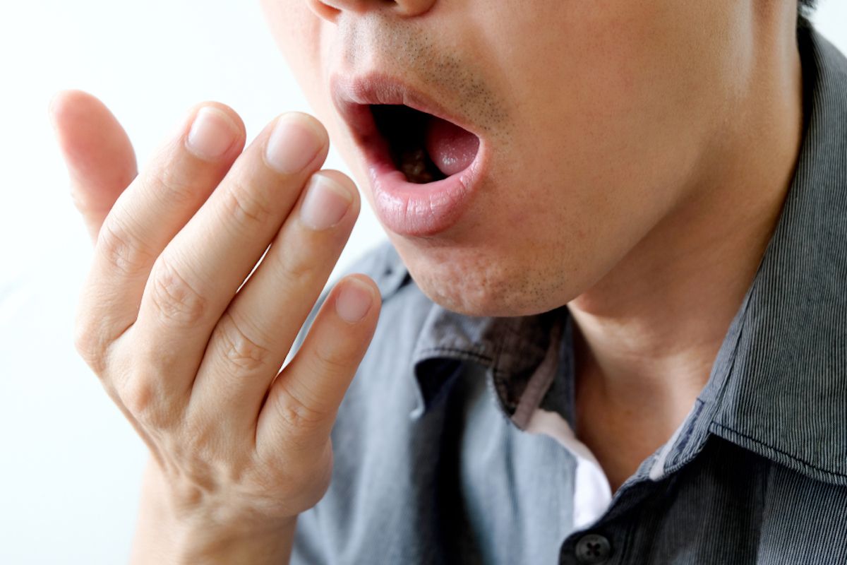 ung mann sjekker for dårlig ånde ved å holde hånden foran munnen og puste
