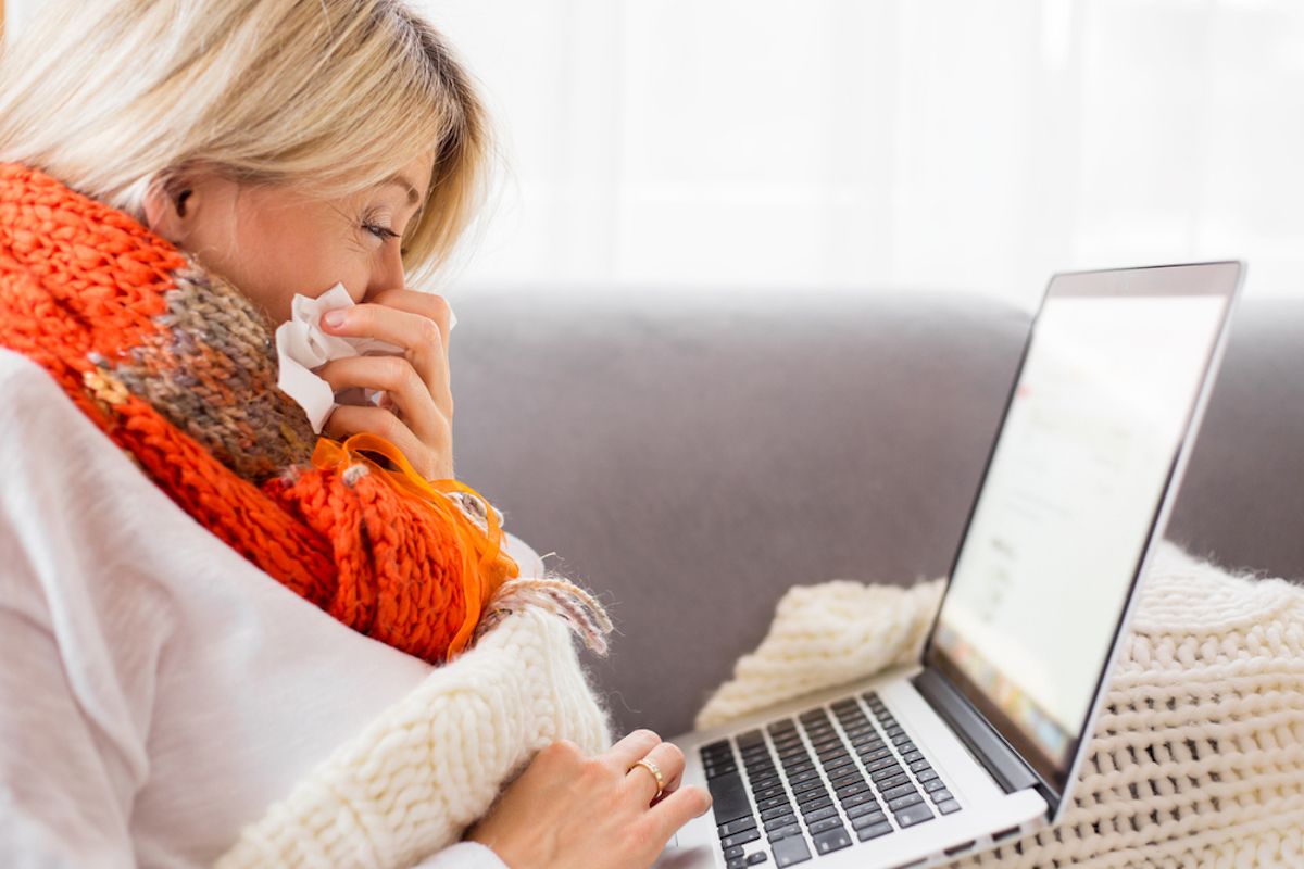 senior donna seduta sul divano utilizzando laptop mentre soffia il naso