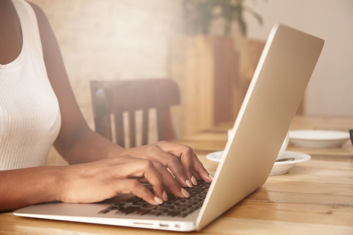 Bàn tay của phụ nữ trẻ da đen ngồi trên bàn sử dụng máy tính xách tay