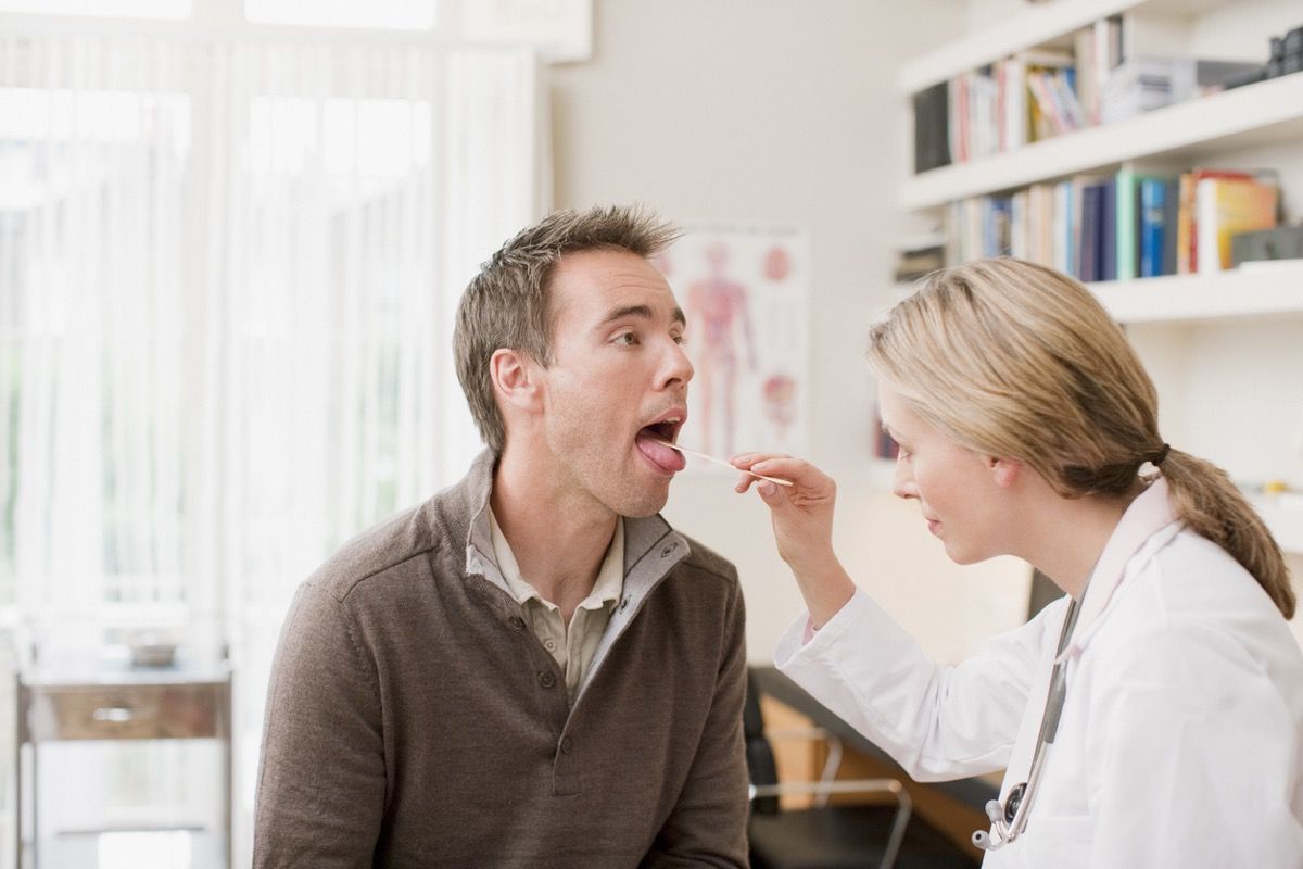 valkoinen naislääkäri käyttää kielen depressoria valkoisella miehellä