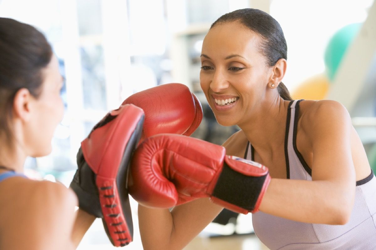 чернокожа жена на средна възраст се усмихва по време на спаринг с боксов партньор във фитнеса