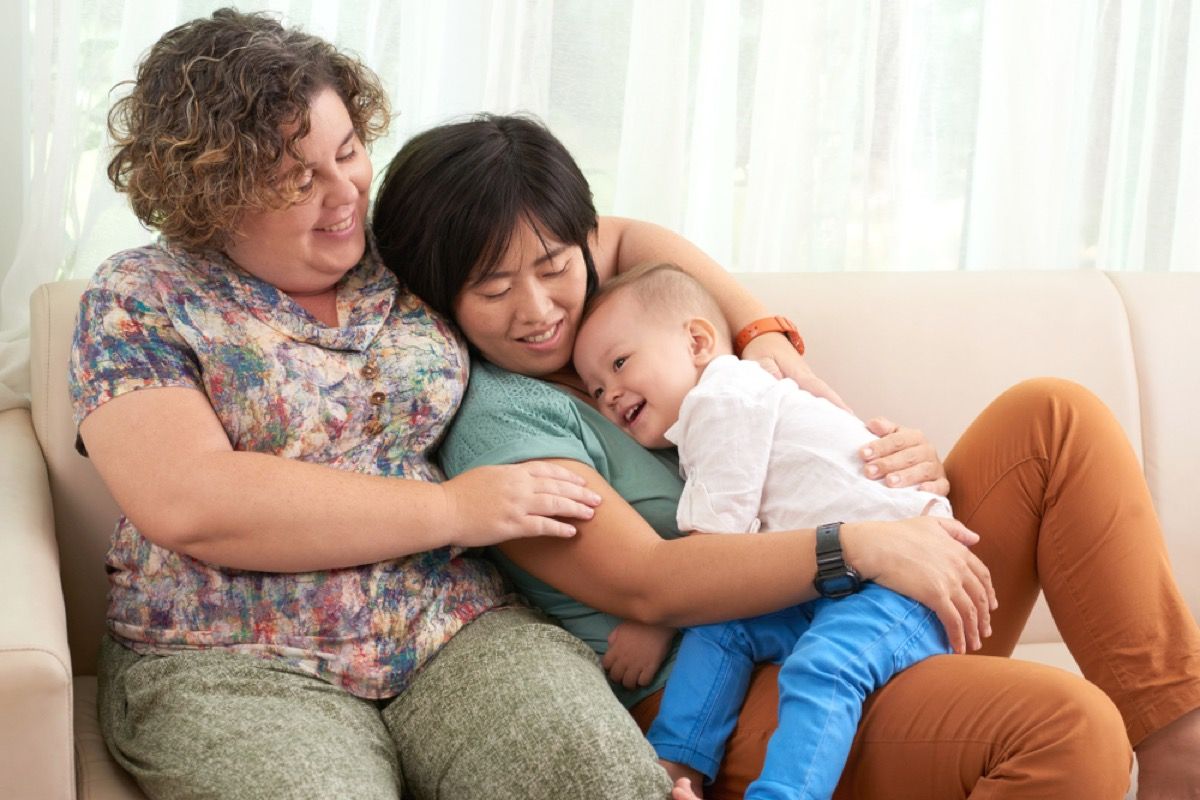 смесена раса лесбийска двойка на средна възраст седи на дивана с бебе
