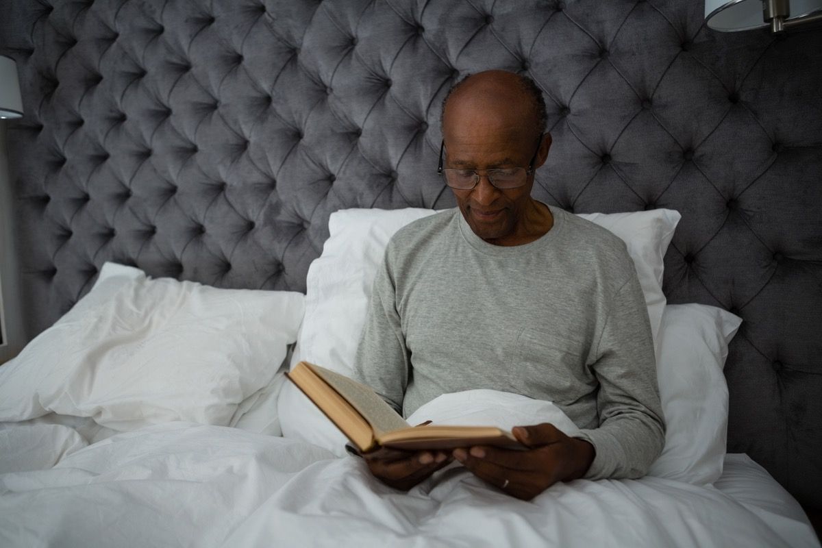 по-възрастен чернокож, който чете книга в леглото