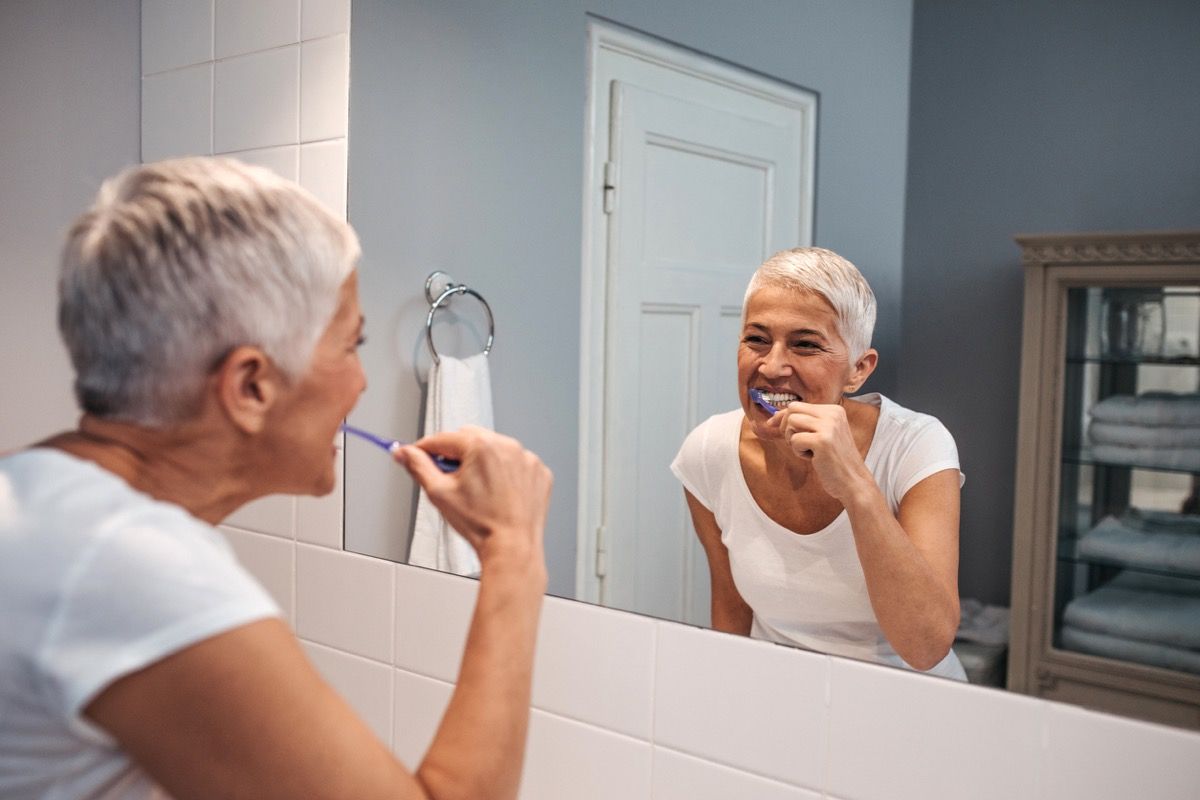 възрастна бяла жена, която си мие зъбите в огледалото