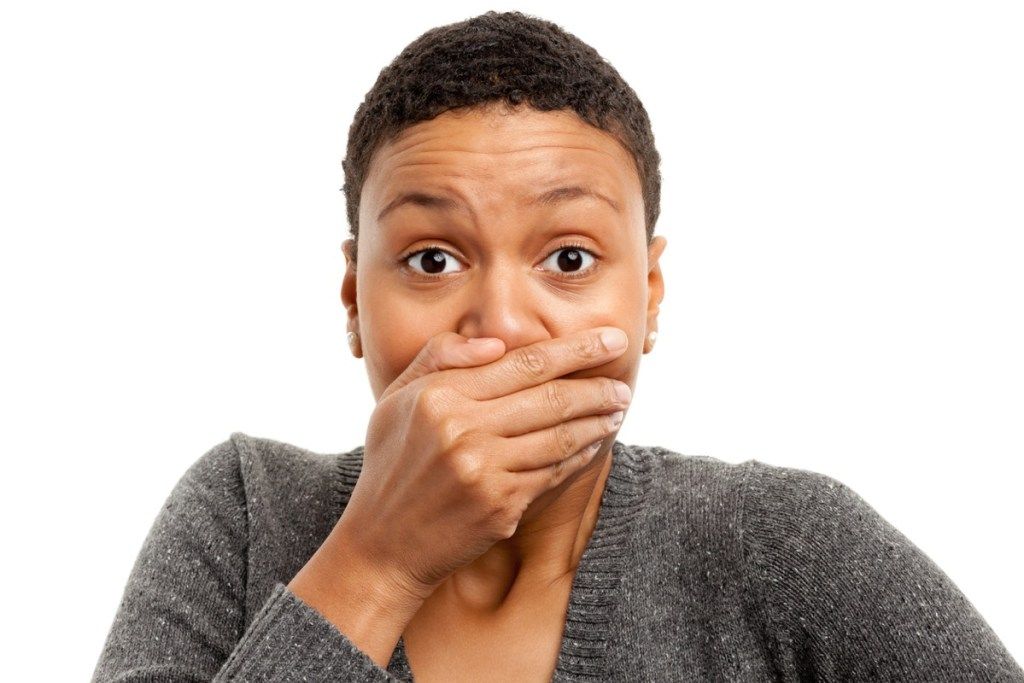 Potret perempuan kulit hitam berlatar belakang putih menutupi mulut dengan tangan