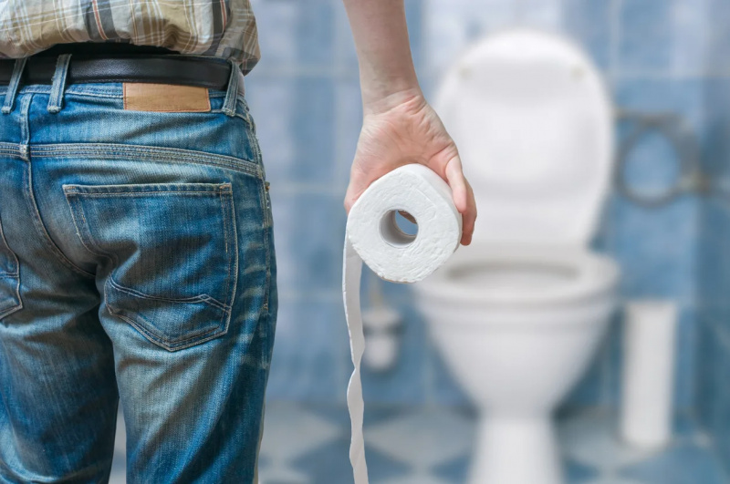   Egy férfi, aki egy tekercs WC-papírt tart a fürdőszobában