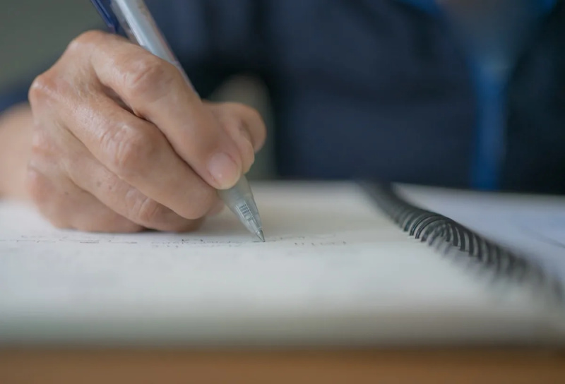   Vanem naise kortsus käsi hoiab pliiatsiga kirjutamise päevikut, kirja või testamenti vihikus. Naispensionär koostab testamendi idee. Vanem ajakirjanik kirjutab aruandeid, memosid või dokumenteerib teavet.