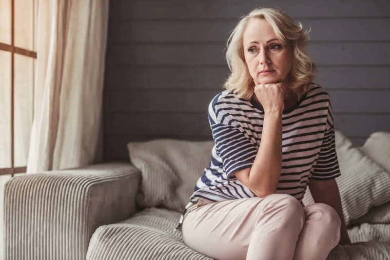   o femeie albă mai în vârstă tristă, așezată pe o canapea