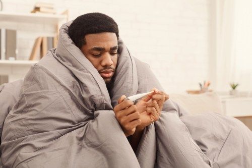 άρρωστος μαύρος κάτω από μια κουβέρτα κοιτάζοντας ένα θερμόμετρο