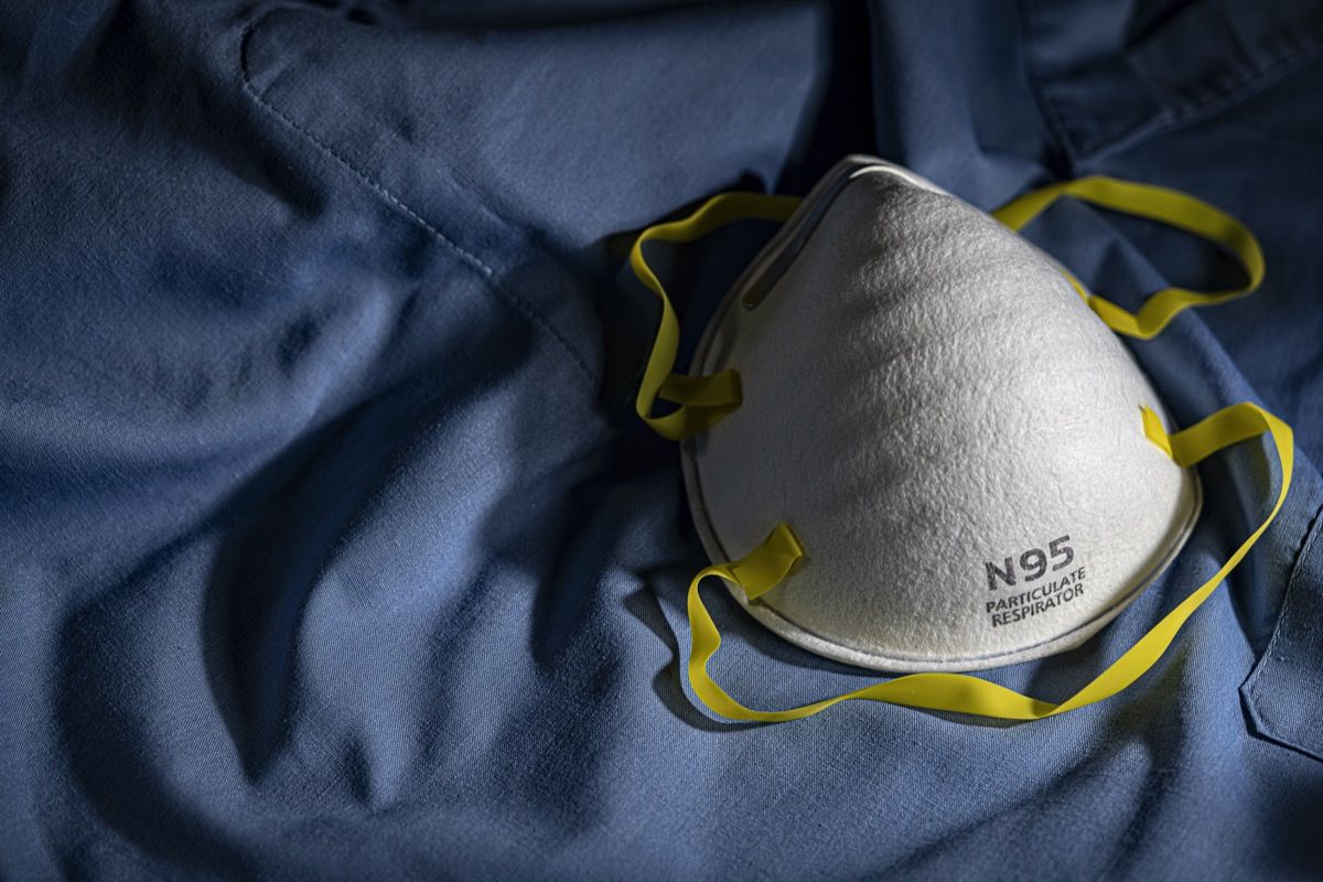 एन 95 पीपीई सुरक्षात्मक मास्क कॉपी स्पेस के साथ नीले मेडिकल स्क्रब पर आराम करता है