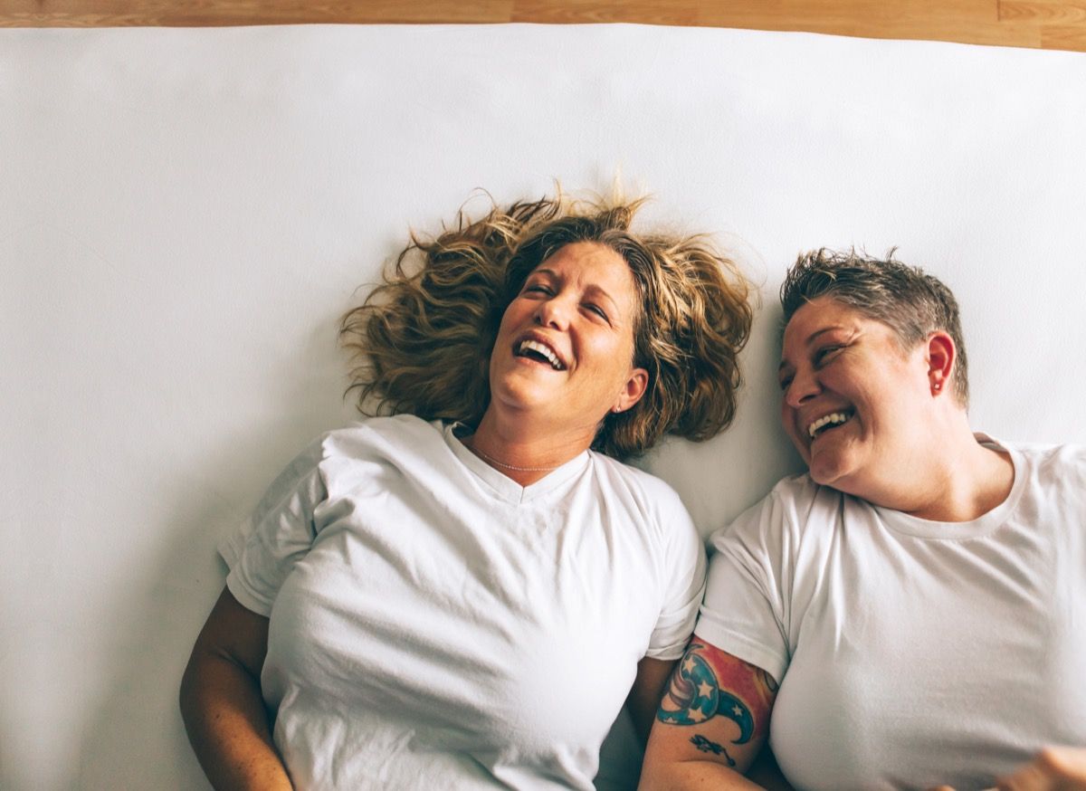 คู่รักเลสเบี้ยนหัวเราะอย่างสนุกสนานขณะนอนอยู่บนเตียงนิสัยหลังจาก 40