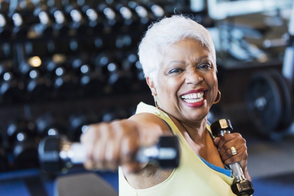 Äldre kvinna som lyfter vikter på idrottshallen