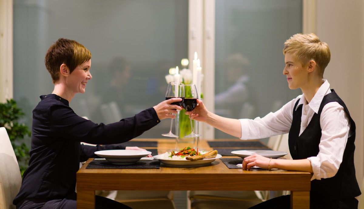 Две белые женщины поджаривают красное вино за едой дома