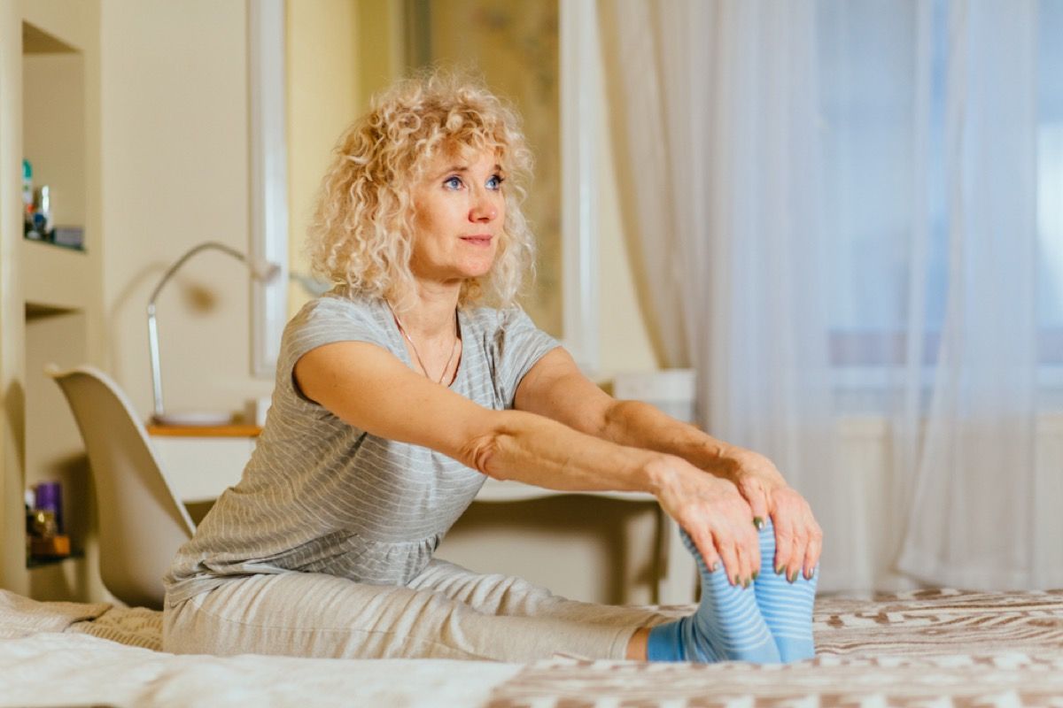 középkorú fehér nő az ágyon nyújtózkodik a lábánál fogva