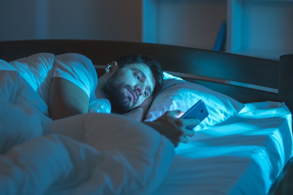 Човекът е сам в леглото и чете своите телефонни промени над 40