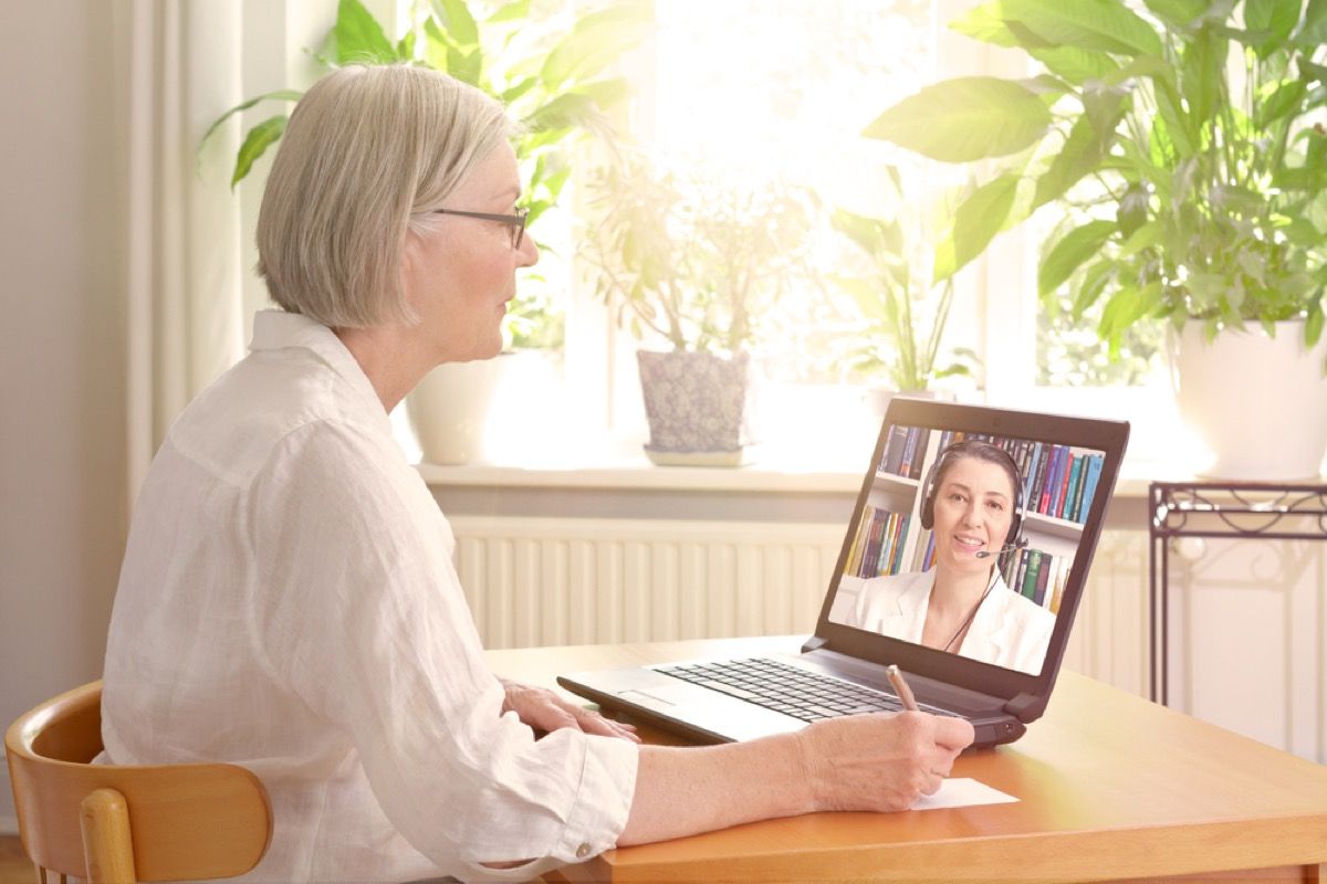 Пожилая белая женщина разговаривает по видео с врачом на ноутбуке
