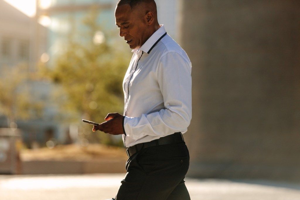 Schwarzer Mann, der sein Telefon betrachtet, während er geht, um gesunder Mann zu arbeiten