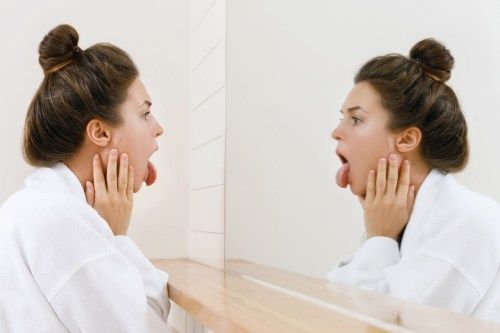 Mujer joven está mirando su lengua en el espejo