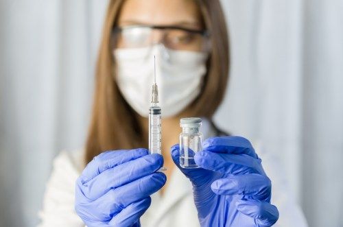 Một nữ nhân viên y tế đeo khẩu trang, kính bảo hộ và găng tay cầm một ống tiêm và lọ vắc xin COVID-19