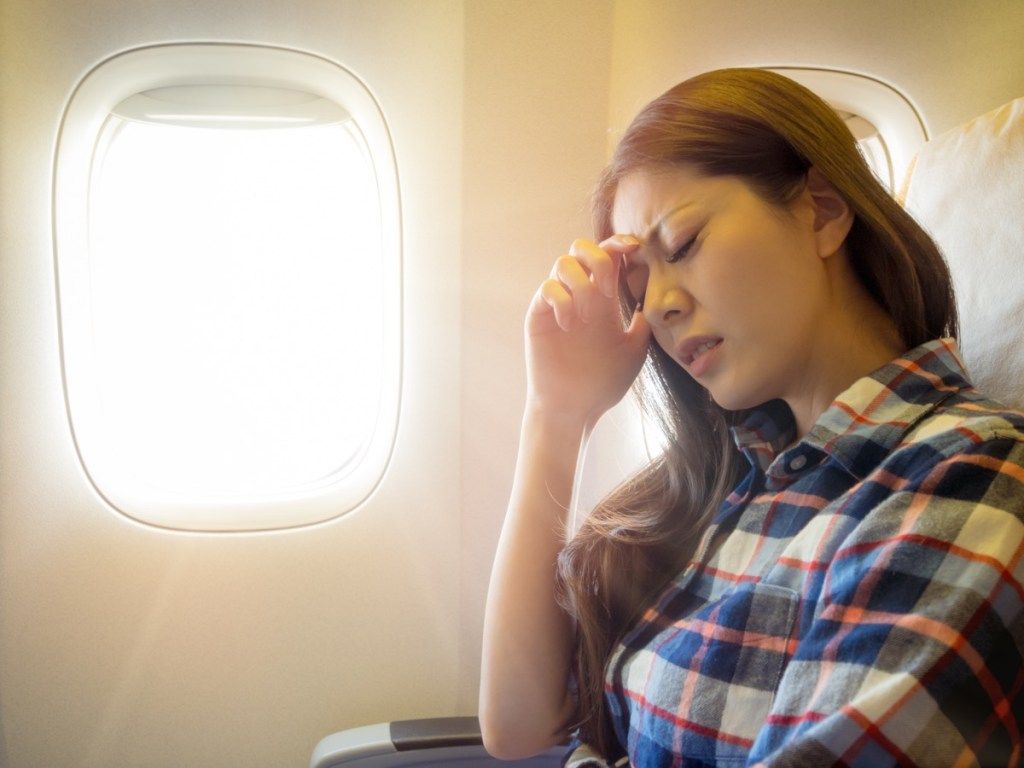 एक हवाई जहाज पर सिरदर्द के साथ अपना सिर पकड़े हुए महिला