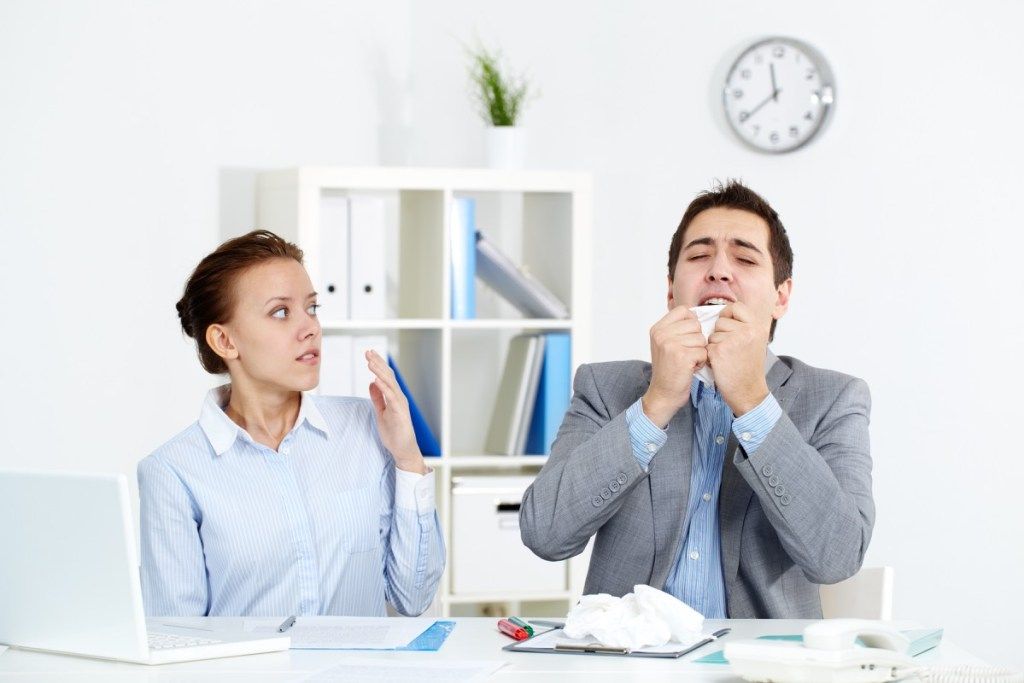 Hombre con resfriado estornudando en el trabajo {Tratamiento del resfriado común}