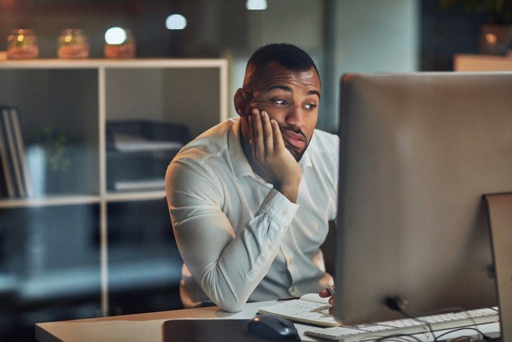رجل يحدق في شاشة جهاز الكمبيوتر الخاص به يشعر بالاكتئاب والقلق يؤذي صحته العقلية