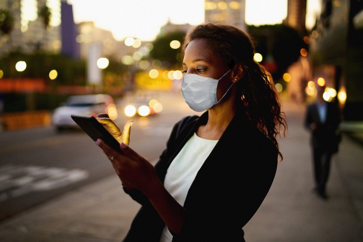 Poslovna žena koja koristi digitalni tablet noću u gradu noseći zdravstvenu masku.